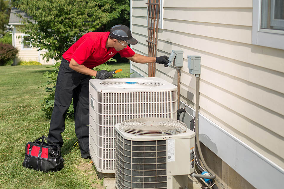 HVAC technician standing next to outdoor heat pump and air conditioner units performing AC maintenance